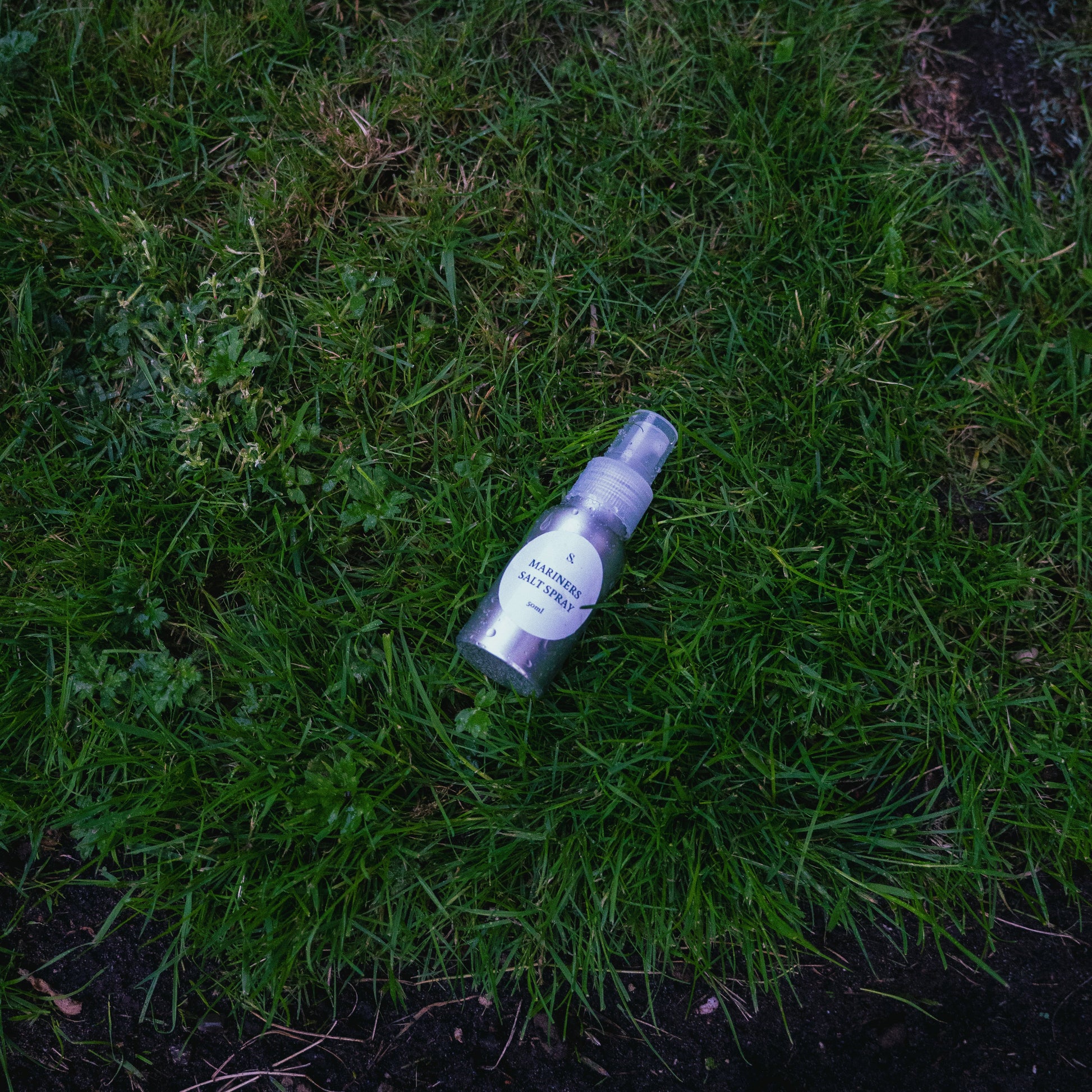 A salt spray bottle with a white label lies on green grass outdoors.
