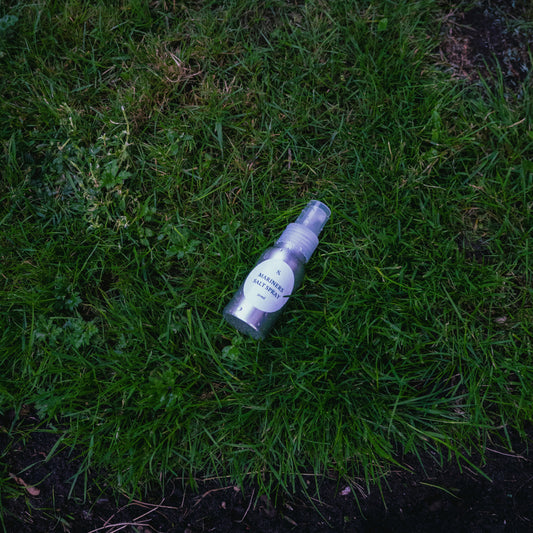 A salt spray bottle with a white label lies on green grass outdoors.