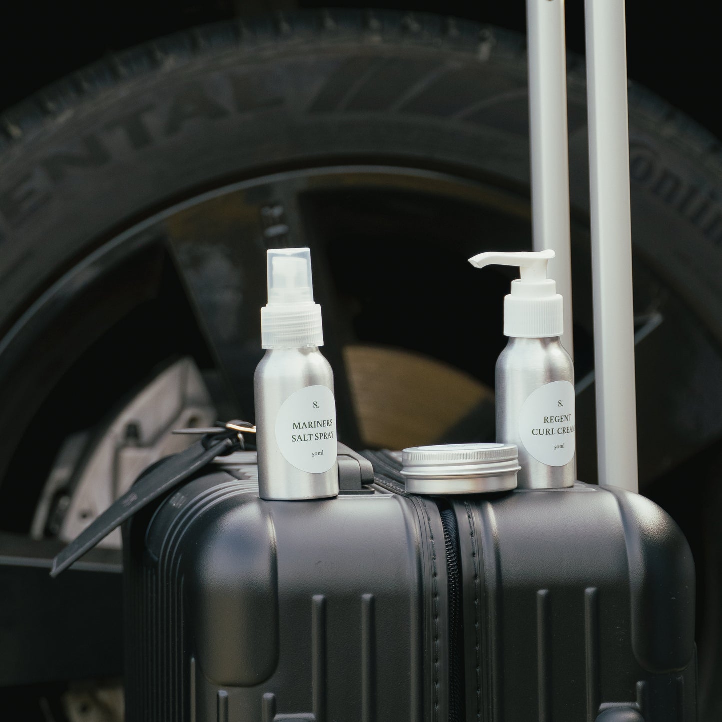Three hair styling travel bottles on a suitcase with a car tire in the background