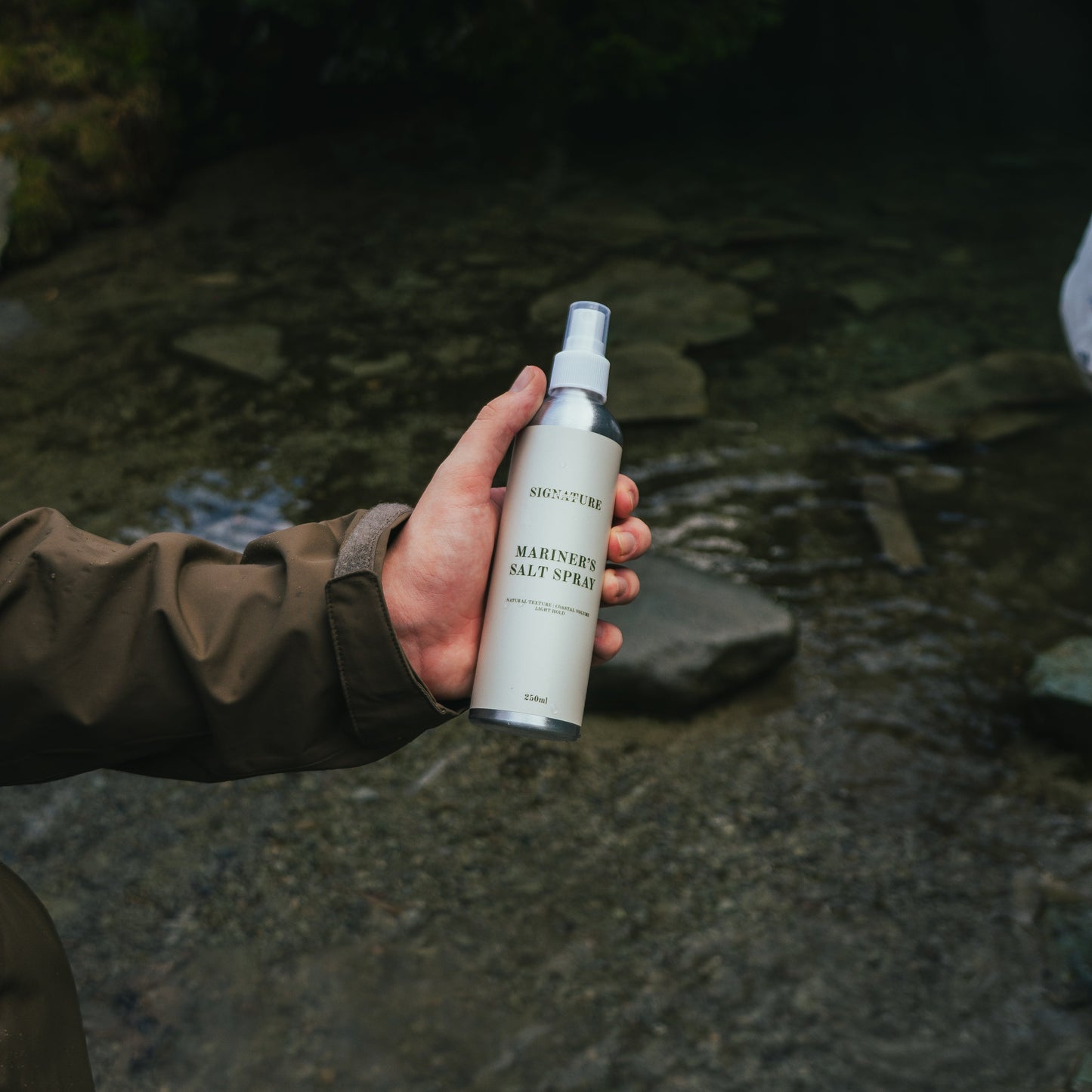 Hand holding a spray bottle labeled 'Mariners' against a natural background