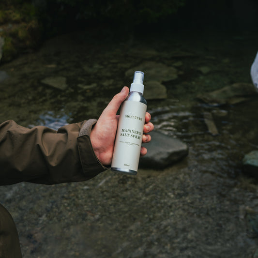 Hand holding a spray bottle labeled 'Mariners' against a natural background