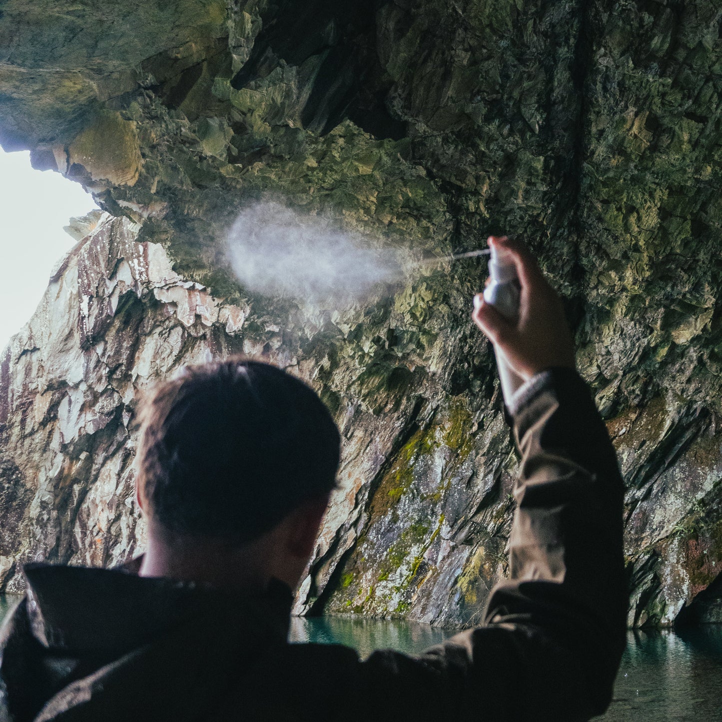Person holding a sea salt spray inside a cave with water and sunlight filtering through