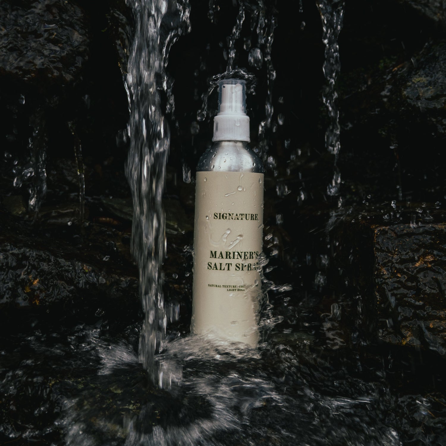 Spray bottle labeled 'Mariner's Salt Spray' on a rocky surface with water flowing.