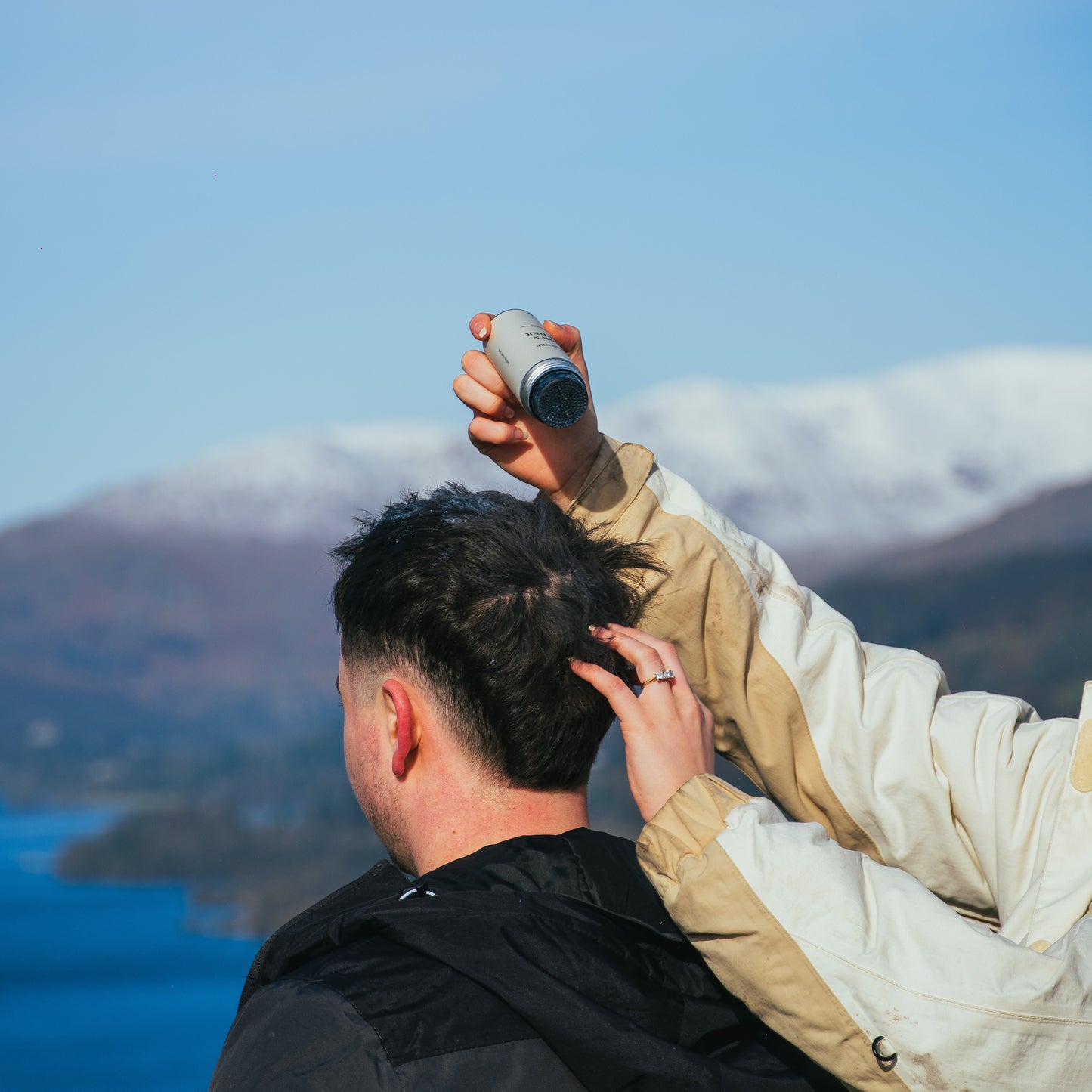 Two people outdoors with a scenic background of mountains and water.