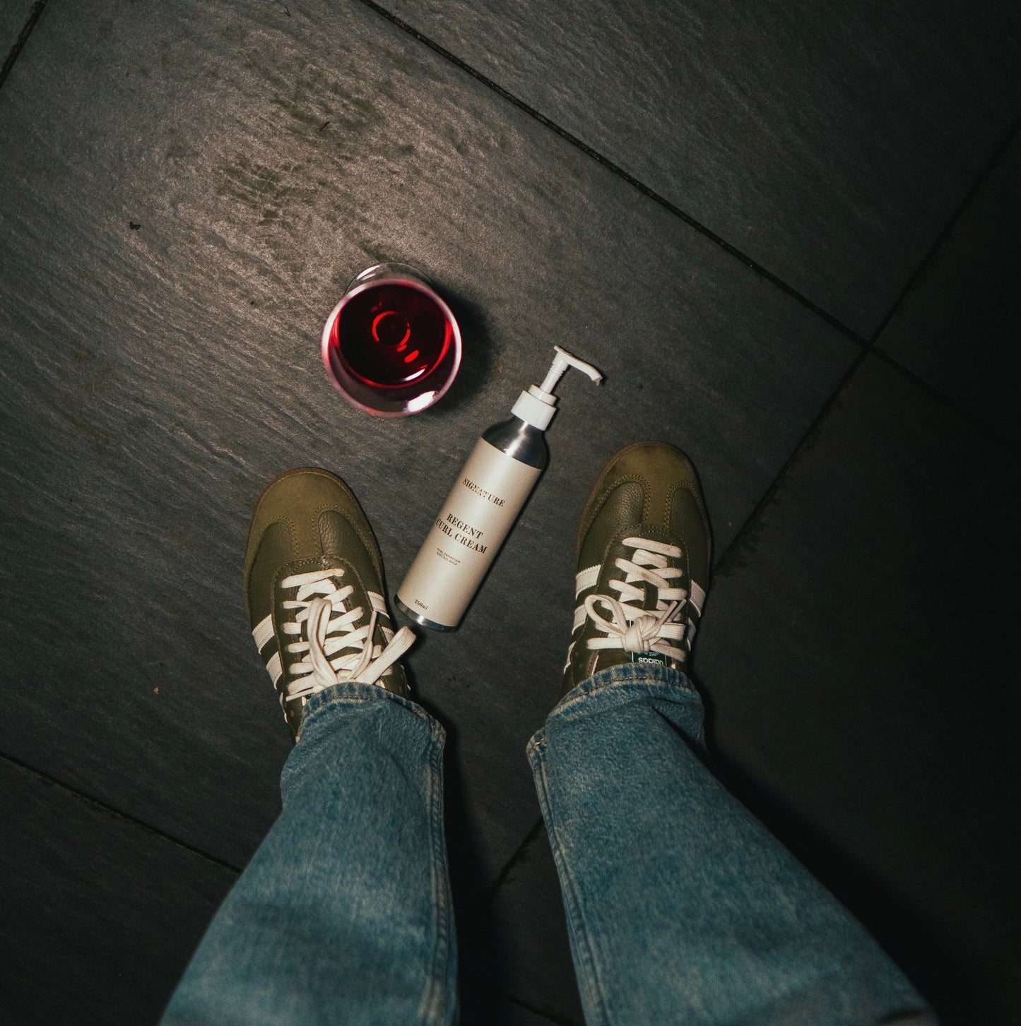 Person wearing shoes and jeans with a bottle and container on a dark floor.