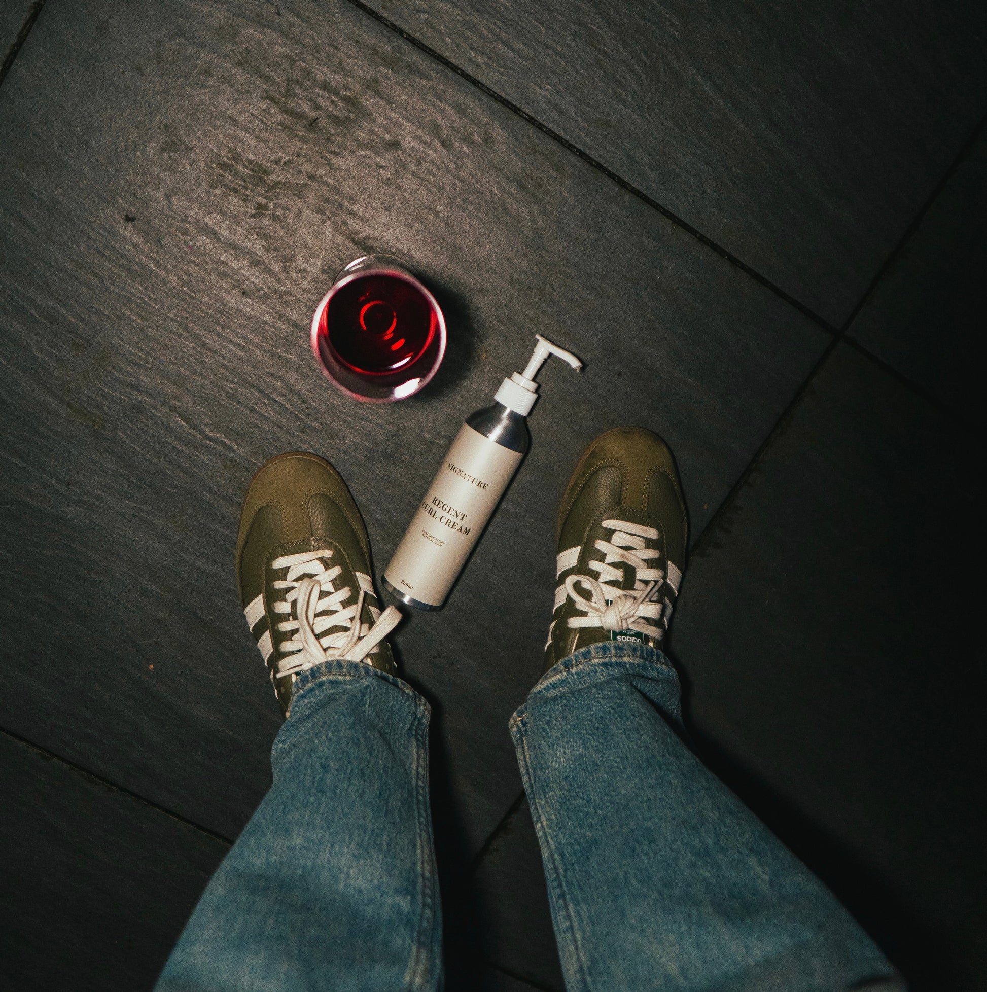 Person wearing shoes and jeans with a bottle and container on a dark floor.