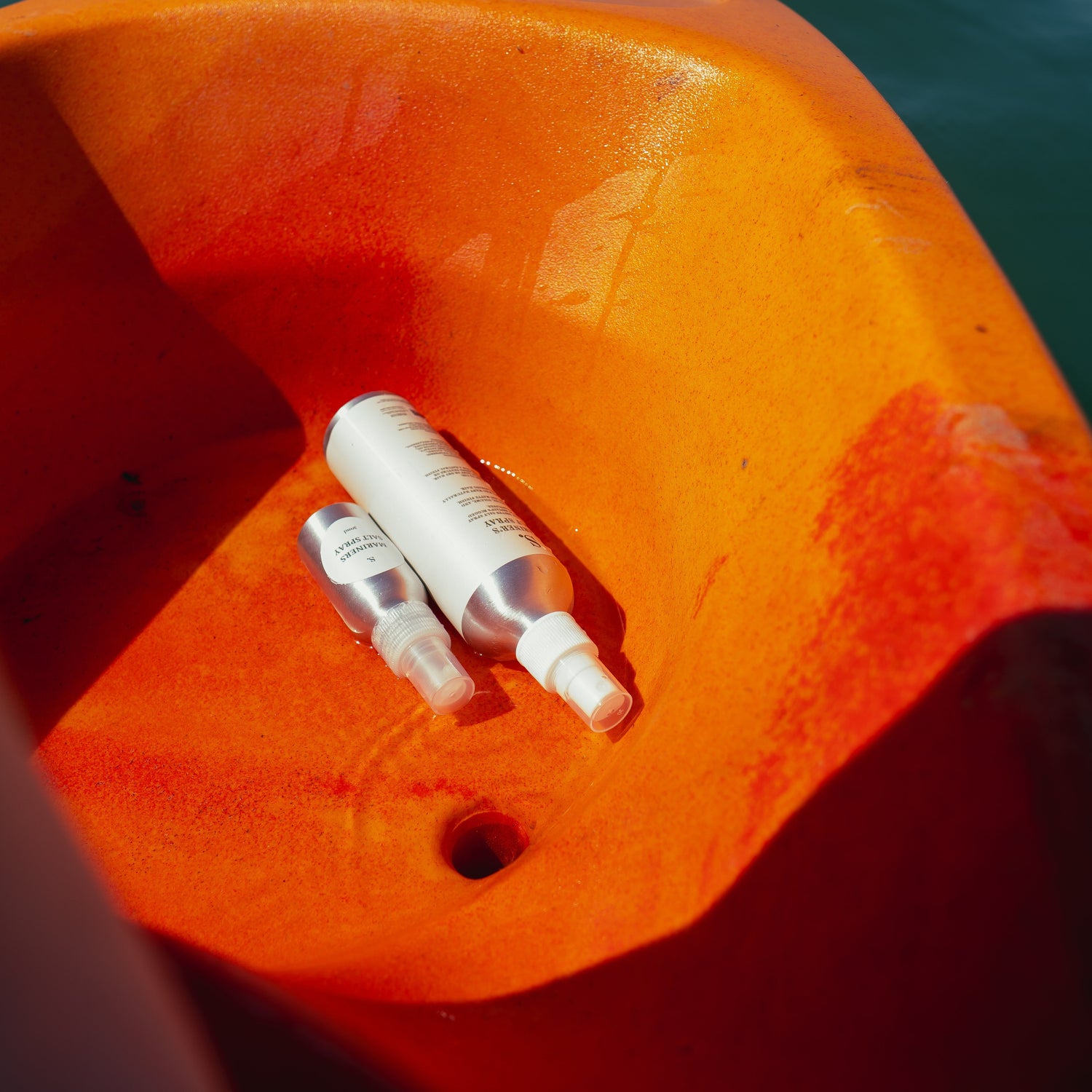 Two white bottles on an orange surface with water in the background
