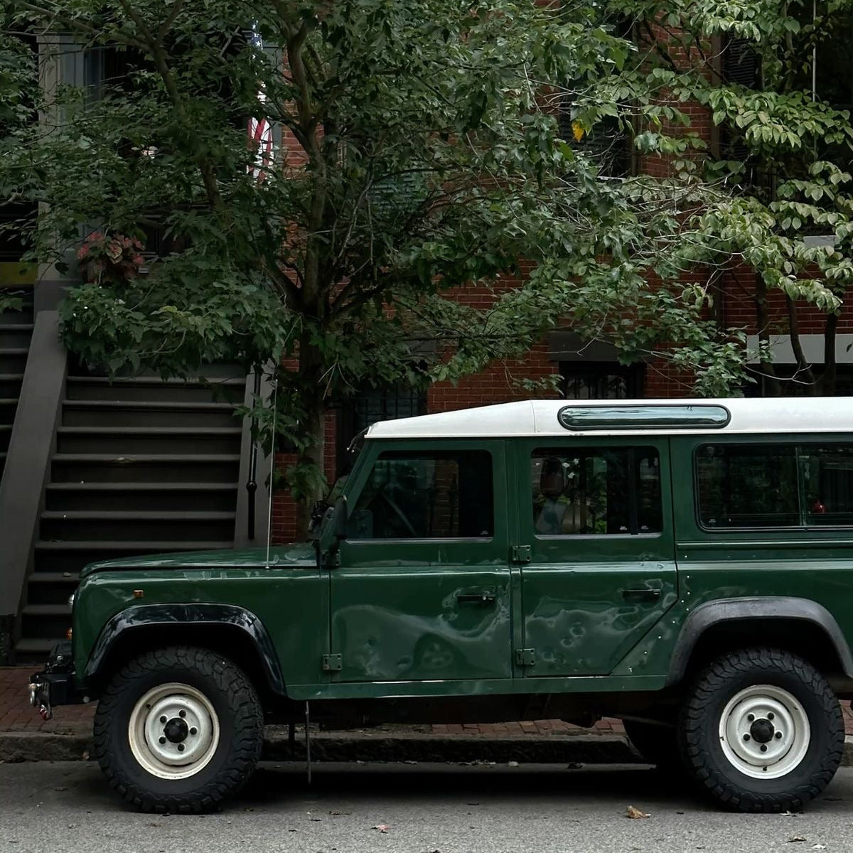 Green Land Rover Defender parked on a street with trees and buildings in the background