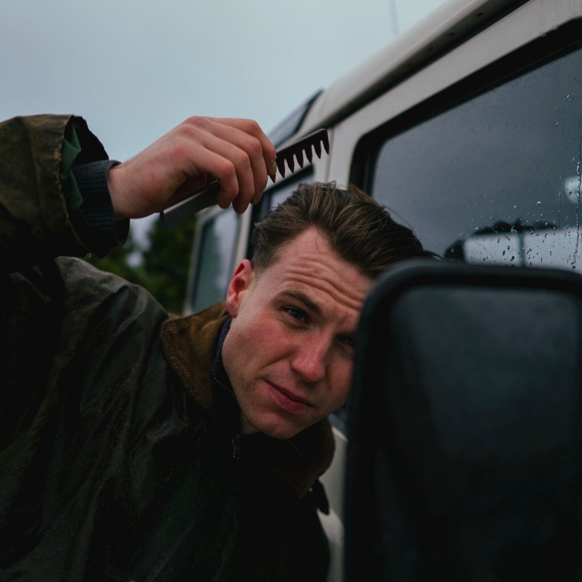 Person combing their hair in front of a car window on a rainy day