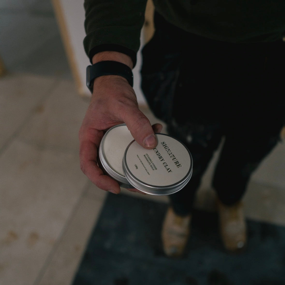 Person holding a hair wax with a label on a blurred background